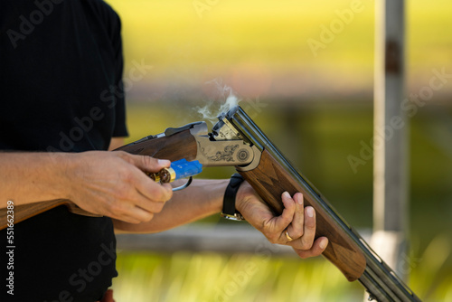 Reloading a gun. Man holding a shotgun round in hand for reloading. Open barrel smoking after a shot. Person practicing skeet shooting sport