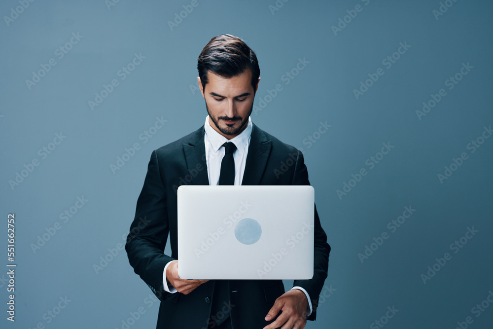 A business man looks at his laptop and works online via the internet in a business suit video call on a blue background A business man looks at his laptop and works online via the internet in a business suit video call on a blue background