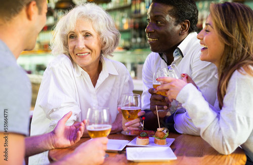 Cheerful family celebrating meeting or acquaintance with beer in nice bar. Focus on elderly woman
