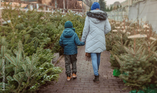 A young mother and her son are buying a Christmas tree. Outdoor Family Choosing Christmas Tree Together.