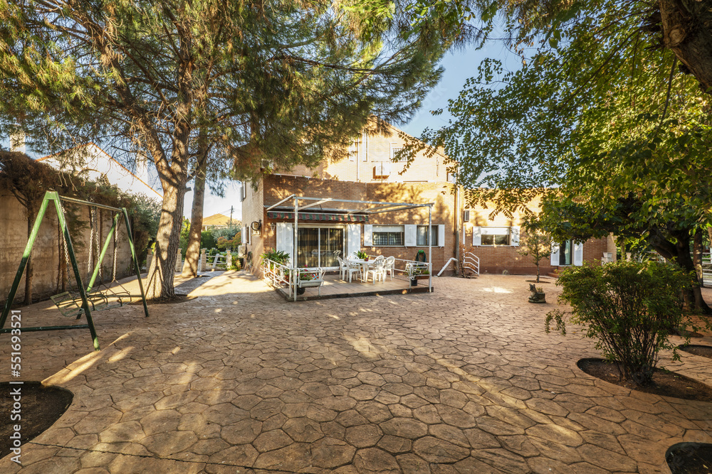 Backyard of a villa with dining room with matching table and chairs and swings for children among the trees