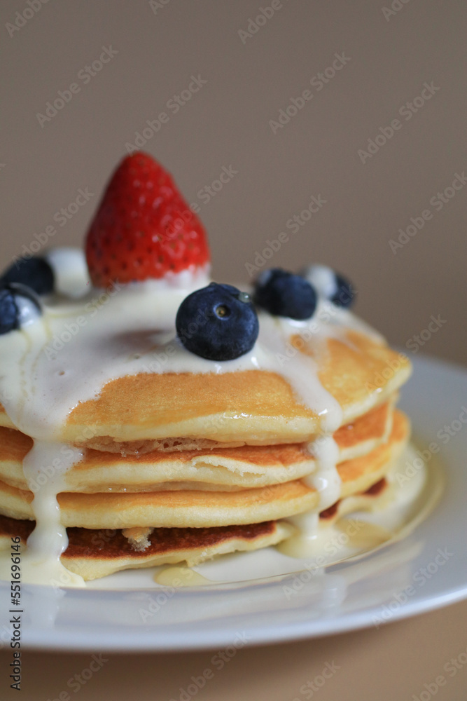Pancakes with blueberries, strawberry and cream. Sweet whipped cream flows from a stack of pancake. Morning tasty homemade breakfast.