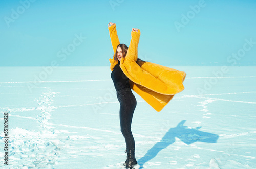 Young happy woman in yellow coat walking on snowy ice, freedom concept
