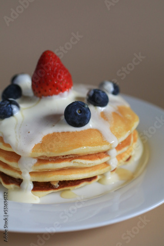 Pancakes with blueberries, strawberry and cream. Sweet whipped cream flows from a stack of pancake. Morning tasty homemade breakfast.