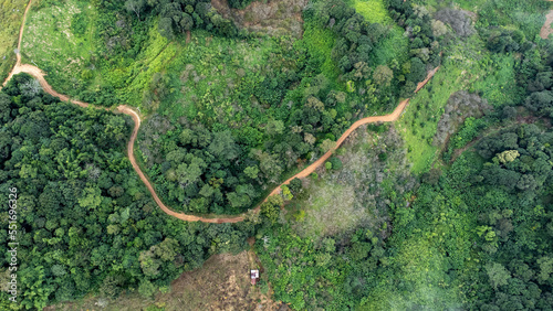 Aerial view from drone of mountain road with sun shining in forest. Top view of a road on a hill in a beautiful lush green forest in Thailand. Natural landscape background.