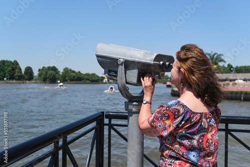 Latin mature woman viewing through public binoculars on the Lujan river bank in Tigre, Buenos Aires, Argentina.