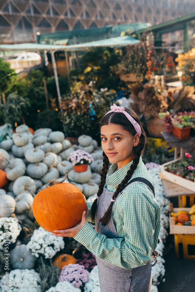Fototapeta premium Happy farmer woman in a denim jumpsuit holds ripe pumpkin