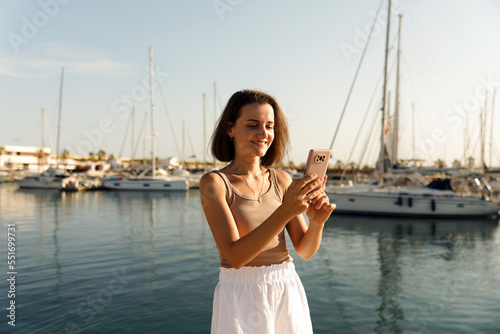 Beautiful woman in talking on the phone against the backdrop of the blue sea and yachts © Enigma