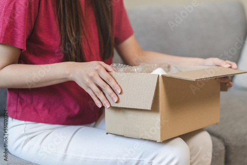 Close-up view of the hands of a young woman opening a cardboard box on the sofa.