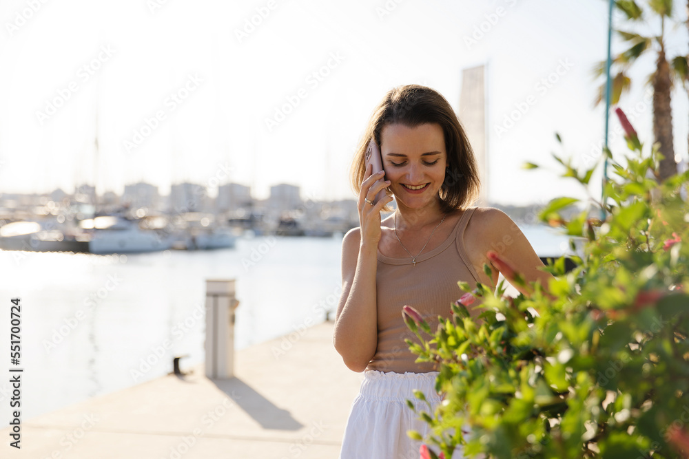 Beautiful woman in talking on the phone against the backdrop of the blue sea and yachts Beautiful woman in talking on the phone against the backdrop of the blue sea and yachts