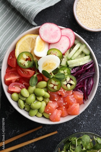 Poke bowl with salmon, edamame beans and vegetables on black table, flat lay