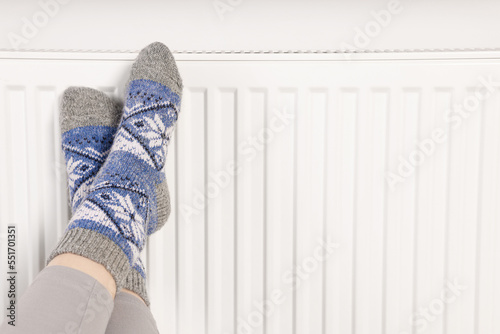 Woman warming feet near heating radiator, closeup. Space for text