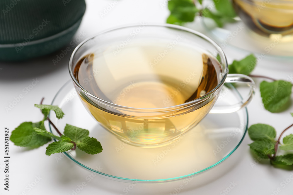 Cup of aromatic herbal tea with mint on white table Cup of aromatic herbal tea with mint on white table