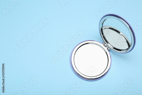 Stylish cosmetic pocket mirror on light blue background, top view. Space for text