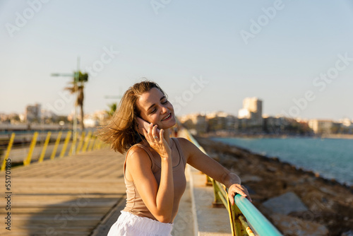 A young stylish woman communicates on a smartphone against the backdrop of a city seascape