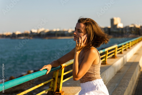 A young stylish woman communicates on a smartphone against the backdrop of a city seascape