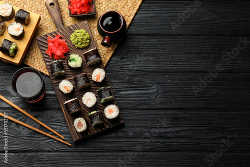Tasty sushi rolls served on black wooden table, flat lay. Space for text