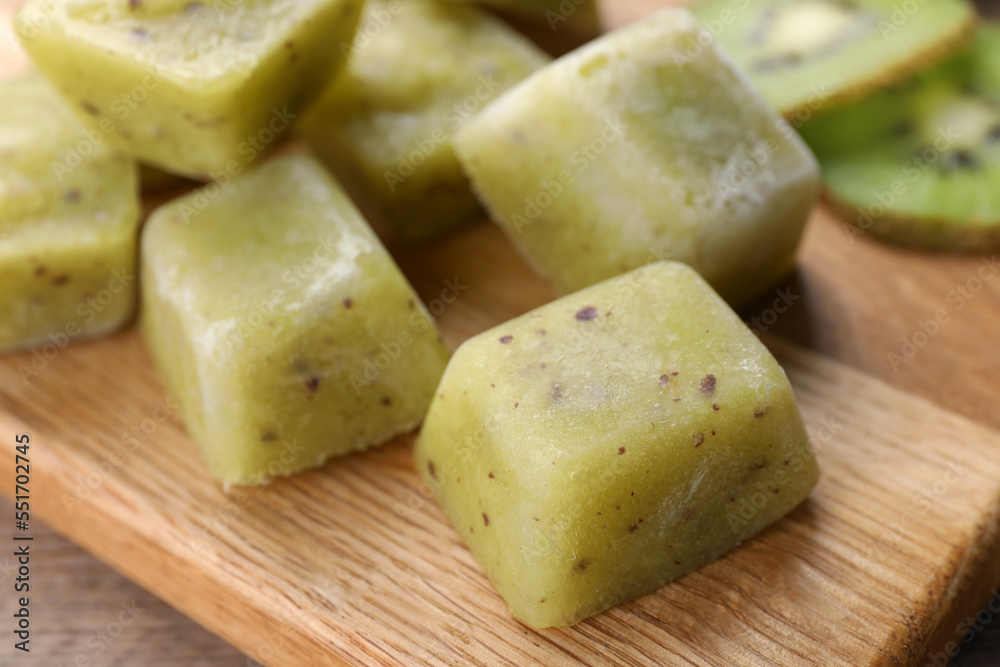 Frozen kiwi puree cubes and ingredient on wooden board, closeup