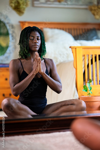 Black woman with green dreadlocks meditating surrounded by plants in her bedroom