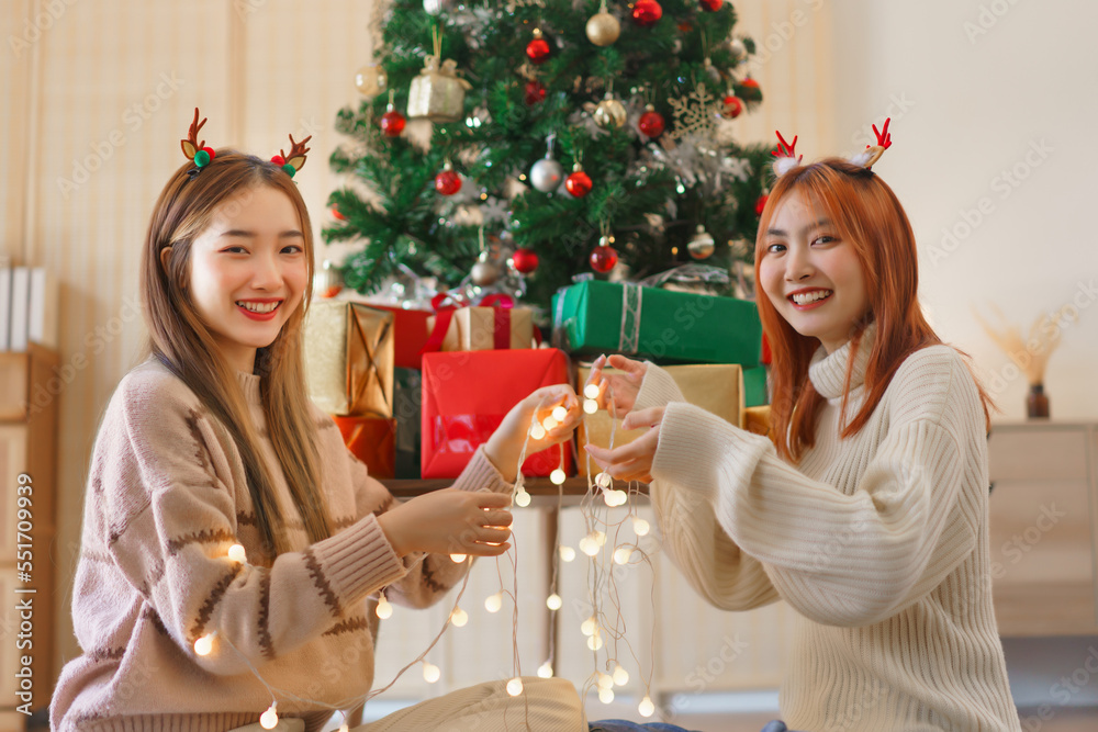 Christmas festive concept, Two women in reindeer horns are holding christmas lights near xmas tree Christmas festive concept, Two women in reindeer horns are holding christmas lights near xmas tree