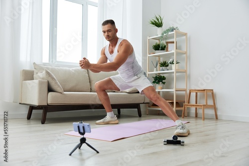 Man sports, watching a workout tape on his phone and repeating exercises blogger, pumped up man fitness trainer works out at home, the concept of health and body beauty
