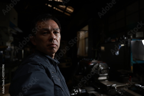 Metalworker in gray work clothes and a lathe in a small to medium-sized small business town factory. Conceptual images of the essence of manufacturing and technical succession. © DRN Studio
