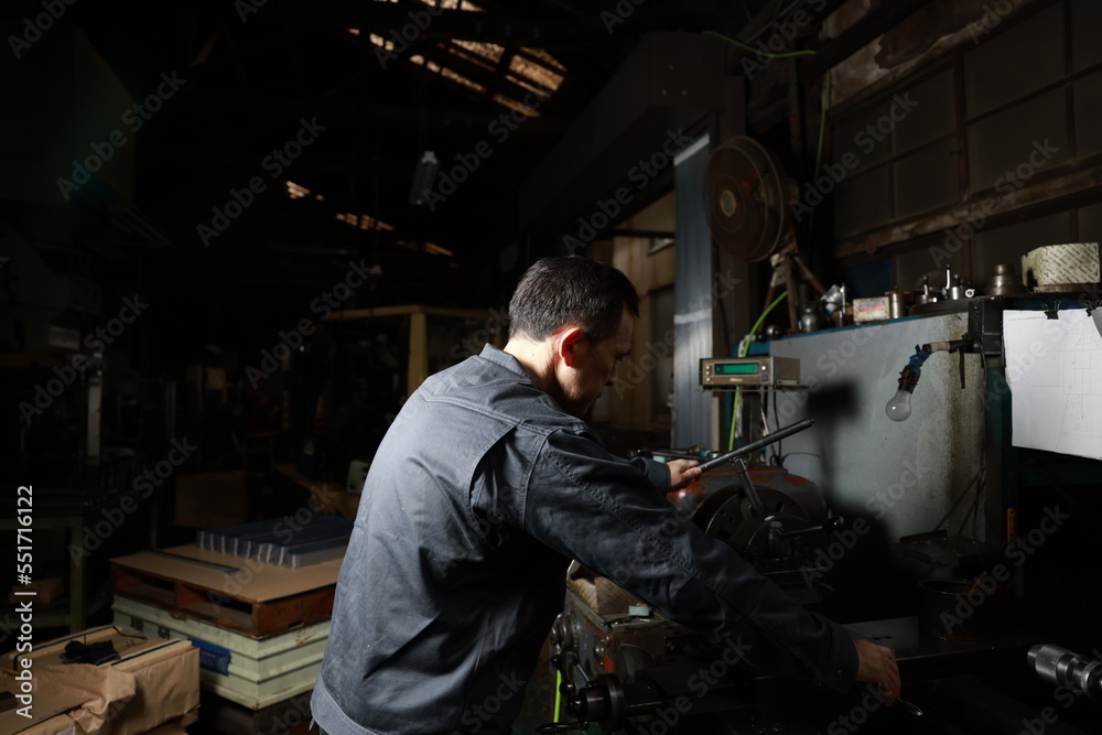 Metalworker in gray work clothes and a lathe in a small to medium-sized small business town factory. Conceptual images of the essence of manufacturing and technical succession.