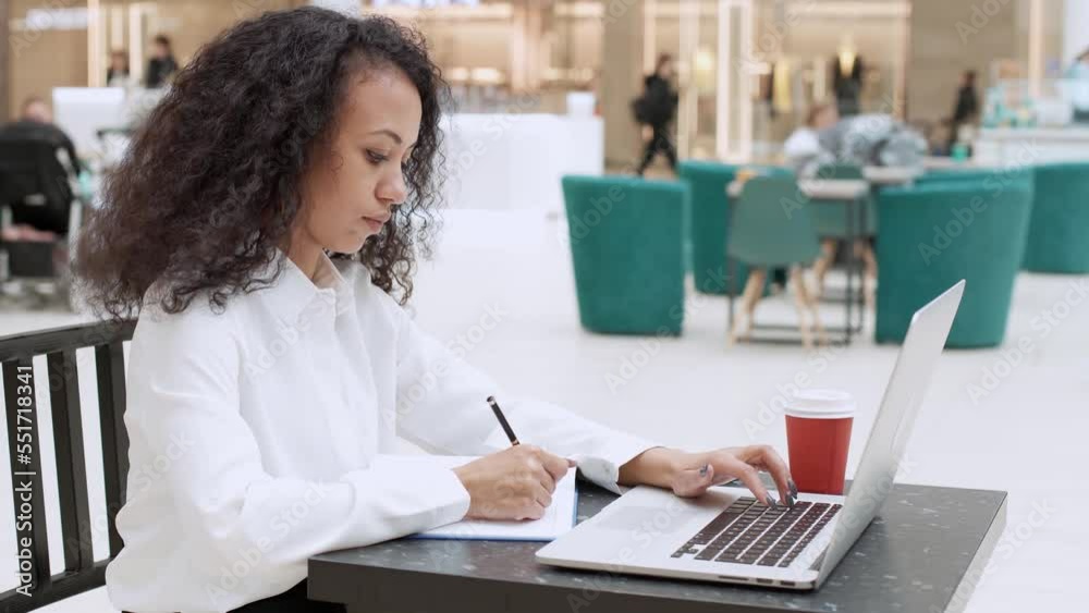 young woman is working on a laptop and taking notes in a notebook. young woman is working on a laptop and taking notes in a notebook.