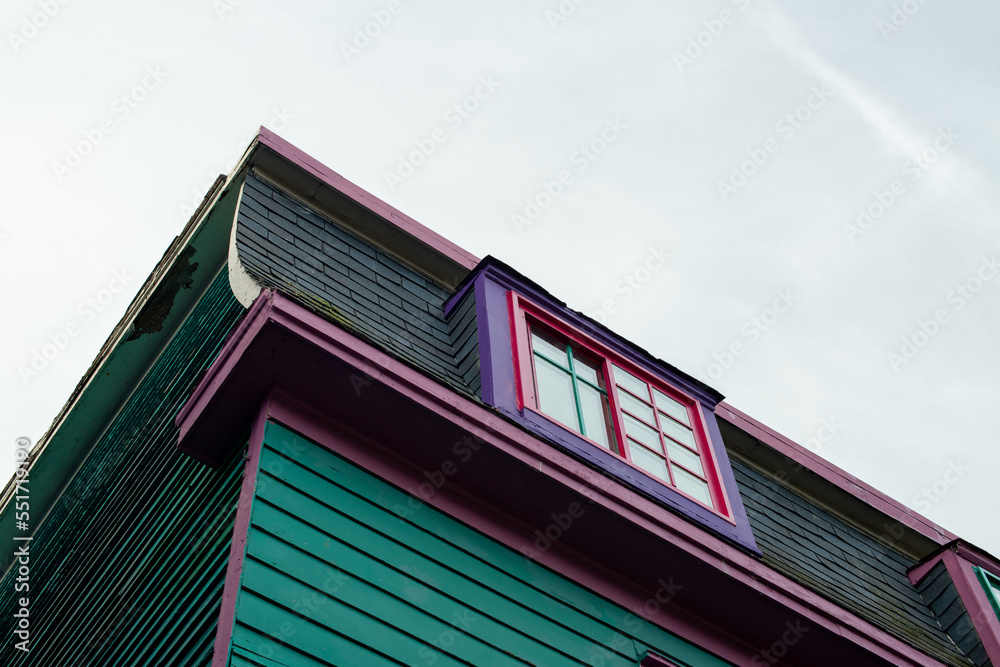 A single four pane Victorian style glass window with a deep pink decorative trim. There's a lace curtain on the inside. The window is in a vibrant mint green narrow clapboard exterior wall of a house.