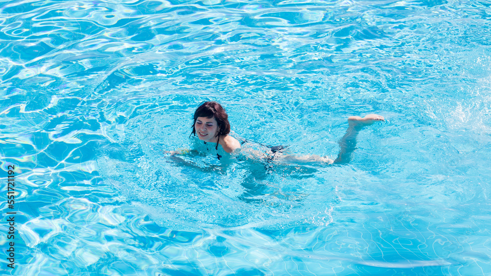 An adult brunette woman is bathing pool with blue clear water.