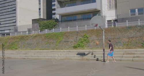 General shot of a young Caucasian man making a layup on a street basketball court. High quality 4k footage.