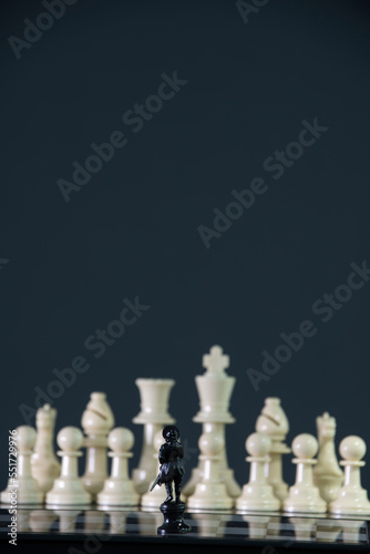 Tiny black figure stands alone facing a group of White set in 2 times size. Both standing against each other on the chess board ready to fight. Size has no matter. Local vs. Global.