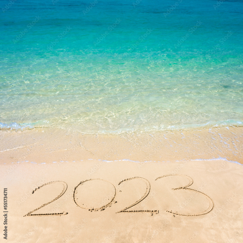 Happy new year 2023 lettering on the beach with wave and clear blue