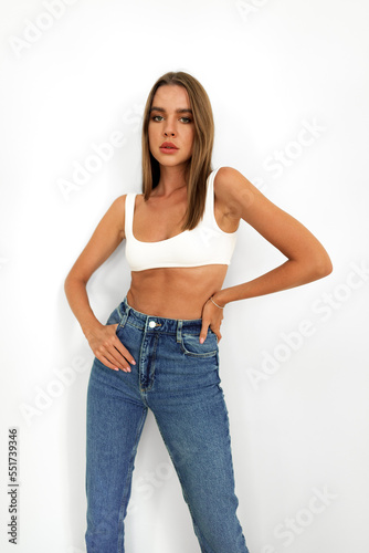 Young model woman in white underwear and jeans posing on studio background