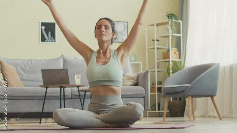 Relaxed young Caucasian woman in activewear practicing yoga meditation on mat at home