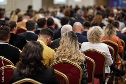 Shallow depth of field (selective focus) details with a crowd of people attending a conference indoors.