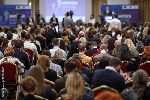 Shallow depth of field (selective focus) details with a crowd of people attending a conference indoors.