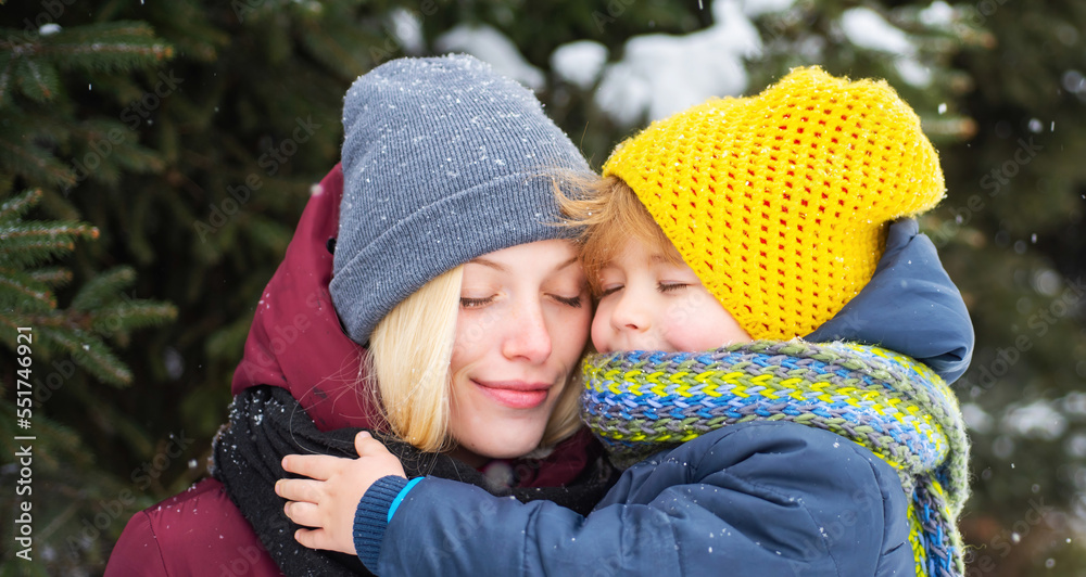 Obraz premium Young mum hugs her pretty kid on winter outdoor. Mother walks with her little son in winter season.