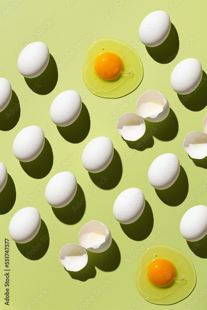 White eggs and egg yolk on a green background. Pattern of eggs. Broken eggs. View from above. White eggs and egg yolk on a green background. Pattern of eggs. Broken eggs. View from above.