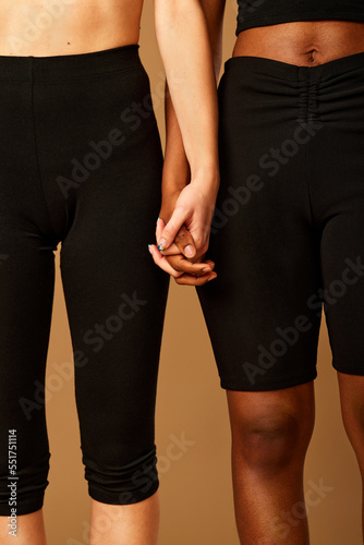 Cropped picture of a two multicultural girls standing in studio in underwear and holding hands.
