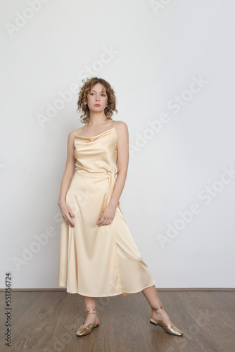 Female model wearing golden camisole silk top and wrapped midi skirt. Stylish monochrome summer outfit. Fashion Studio shot.