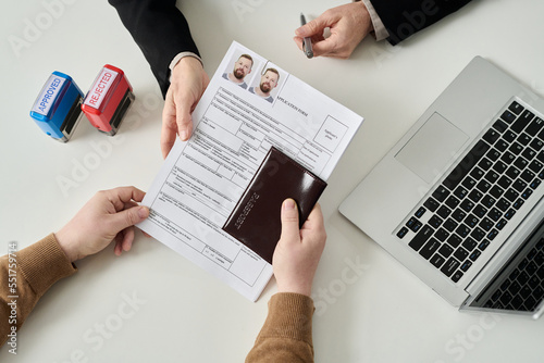 Top view of unrecognizable man applying for visa in immigration office and handing documents to worker