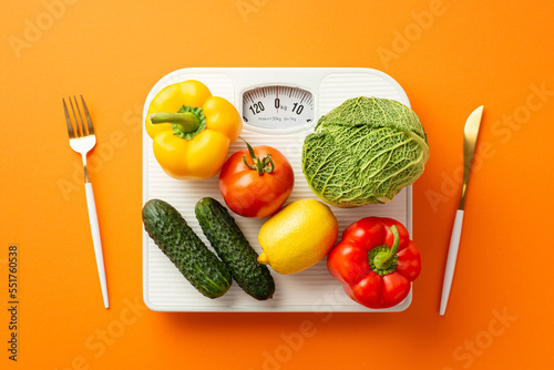 Proper diet concept. Top view photo of vegetables on scales knife and fork on isolated orange background