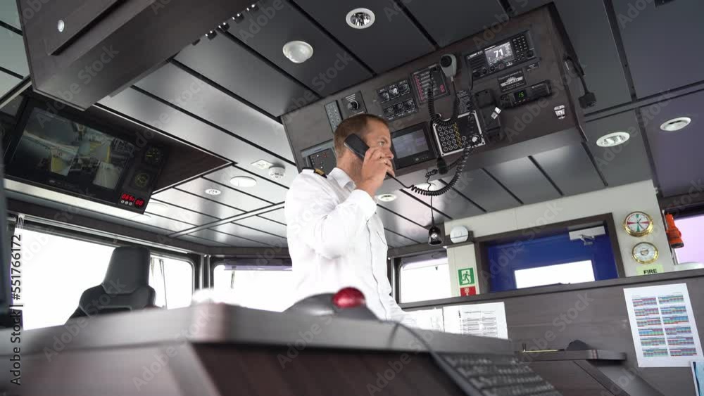 Ships captain talking in vhf radio in modern wheelhouse - Static low angle clip with blurred navigation console in foreground and male captain in middle of wheelhouse