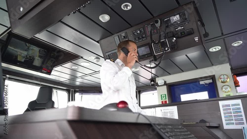 Ships captain talking in vhf radio in modern wheelhouse - Static low angle clip with blurred navigation console in foreground and male captain in middle of wheelhouse photo