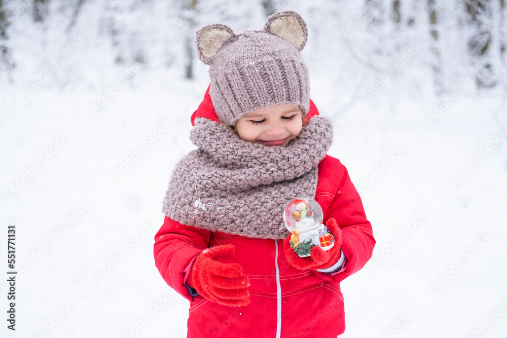 cute kid girl in pink snowsuit and knitted hat and scarf holds snow ball in winter forest cute kid girl in pink snowsuit and knitted hat and scarf holds snow ball in winter forest