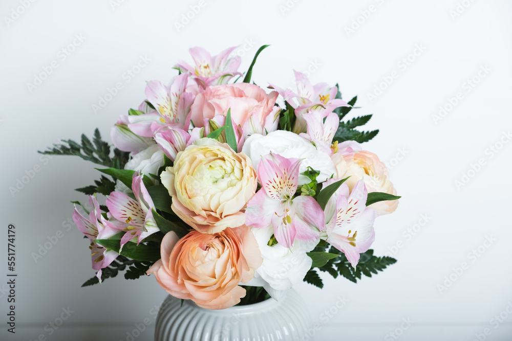 Beautiful bouquet of fresh colorful pastel ranunculus and lily flowers in full bloom with green fern leaves in vase against white background, close up. Spring bunch of buttercups.