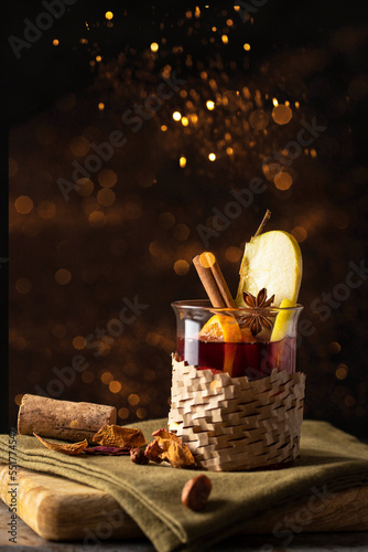 Fototapeta Naklejka Na Ścianę i Meble -  Christmas drink. Mulled wine  decorated with apple and with spices on wooden cut board witj golden bokeh. Winter time beverage  concept.