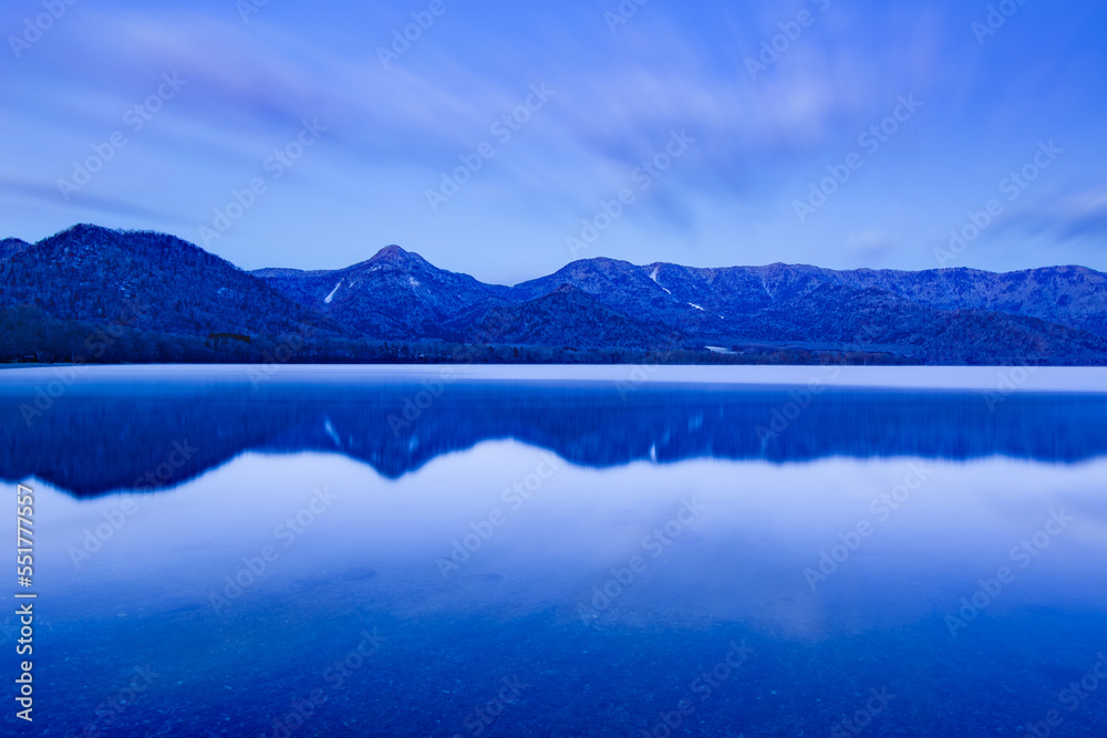 淡いブルーに染まる薄明りの湖の水面に映る山と空。