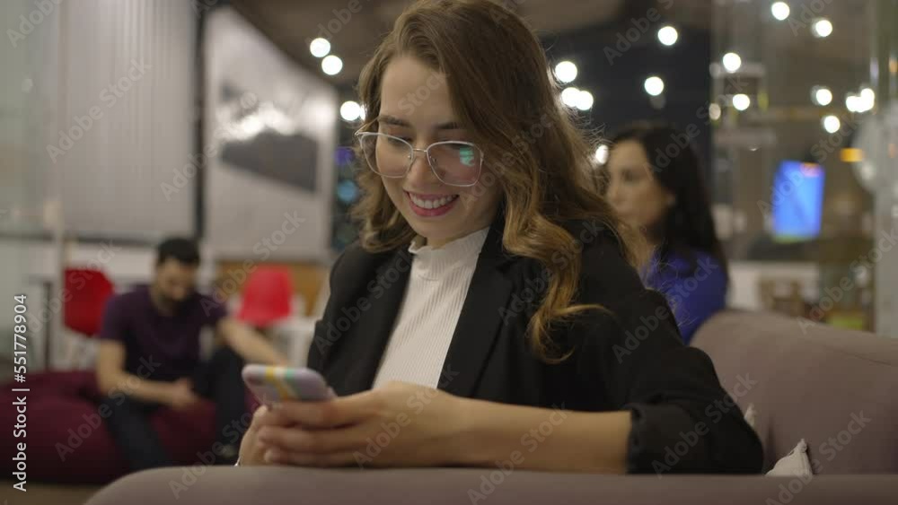 Happy young millennial woman typing message on smartphone device smiling at night. Adult girl holding phone texting message or reading notification